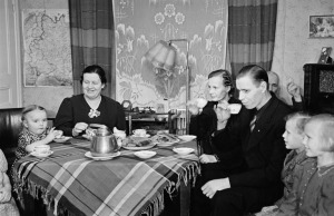 1942 . Kutsut kotona, henkilöitä kahvipöydän ääressä, taustalla oikealla mies savuke kädessään.